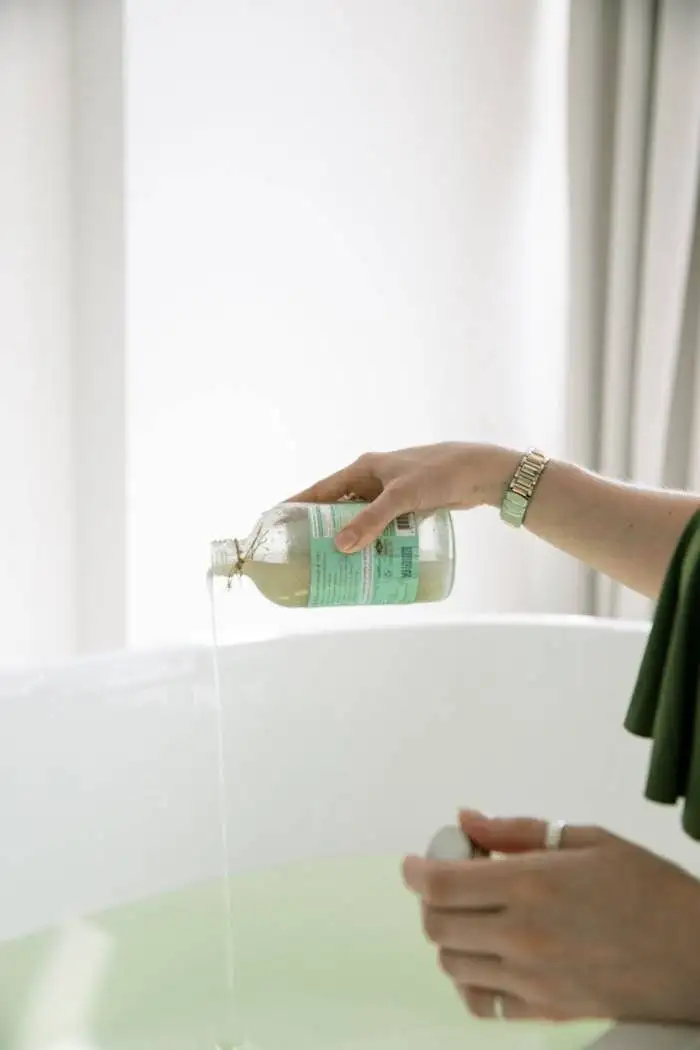 A woman pouring aromatherapy bath oil into a bathtub for a relaxing skincare routine.