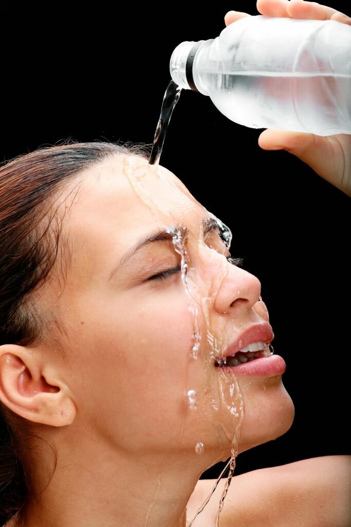 A happy woman splashing water on her face, representing clean and balanced skin after a proper routine.
